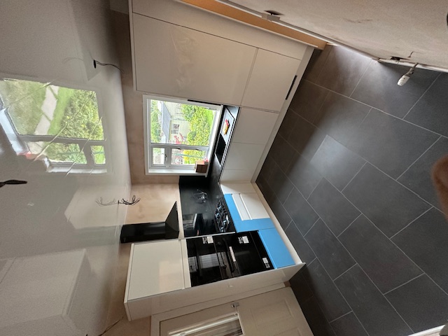 Contemporary kitchen with handleless white cabinets and dark tiles